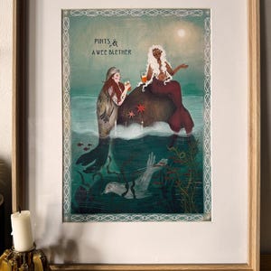 May include: A framed art print featuring a selkie and a mermaid sitting on a rock in the ocean, both holding glasses of beer. The text "PINTS & A WEE BLETHER" is printed above them. The scene includes a swimming seal, seaweed, and starfish.