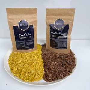 May include: Two brown paper bags with labels that say "Bee Pollen" and "Raw Bee Propolis". The bags are sitting on a white plate with a pile of yellow bee pollen on the left and a pile of brown bee propolis on the right.