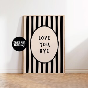 May include: A framed art print with a black and white striped background. The print features an oval shape with the words "LOVE YOU, BYE" in black text. The oval is outlined with a dotted border. The frame is a light wood color.