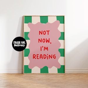 May include: A framed print with a green and white chequered pattern. The pink central shape features the red text "NOT NOW, I'M READING". A black circle with white text "FREE UK Delivery" is in the lower left corner of the print.