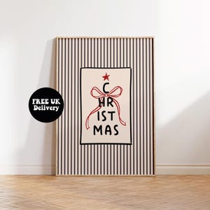 May include: A framed art print with a Christmas theme. The artwork displays the word "CHRISTMAS" in a playful font, with a red bow and star design. The background has vertical black and white stripes.
