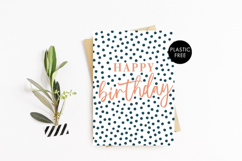 May include: A white card with a blue polka dot pattern and the text "Happy birthday" in pink lettering. The card is on a brown envelope and a white surface.