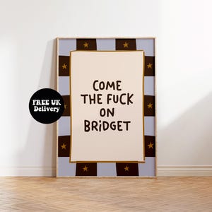 Op de afbeelding: Een ingelijste kunstdruk met de tekst "COME THE FUCK ON BRIDGET" in het zwart. De print heeft een lichtbeige achtergrond en is omlijst met een lichtblauwe rand met bruine vierkanten en gouden sterren. Een zwarte cirkel met witte tekst staat in de hoek.