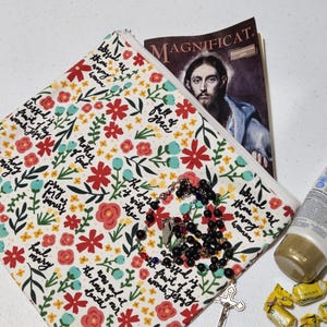 May include: A floral print zippered pouch with a rosary, a magazine with a religious image, a tube of lotion, and wrapped candies. The pouch has a white background with red and blue flowers and script.