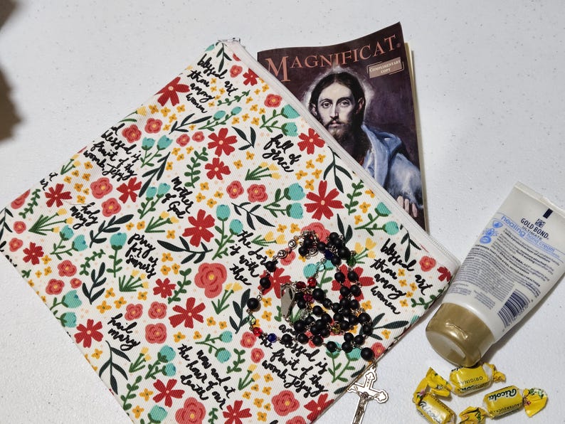 May include: A floral print zippered pouch with a rosary, a magazine with a religious image, a tube of lotion, and wrapped candies. The pouch has a white background with red and blue flowers and script.