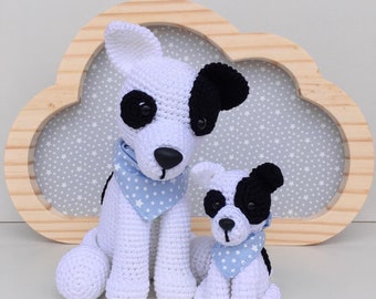 May include: Two crocheted dog plushies, one larger than the other, both white with black patches and blue and white star-patterned bandanas. The plushies are sitting in front of a wooden cloud-shaped frame with a light blue background.