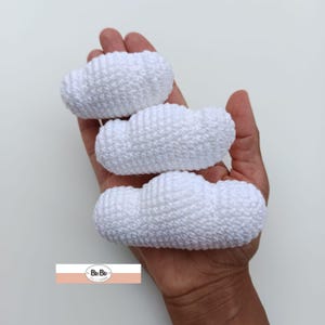 May include: Three white crocheted clouds of varying sizes, held in a hand.