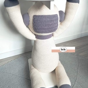 Pode incluir: Uma mesa de crochê artesanal e extravagante em forma de astronauta de desenho animado. A mesa apresenta um tampo branco sustentado por um corpo creme com detalhes cinzentos. Os braços e pernas do astronauta formam a base, criando um móvel único.