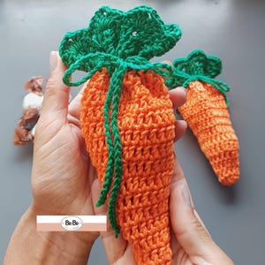 Pode incluir: Duas bolsas de crochê em forma de cenoura com topos verdes. As bolsas são feitas com fio laranja e verde.