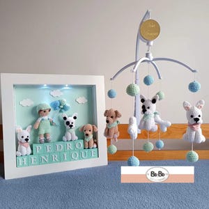 Peut inclure: Mobile et œuvre d'art encadrée pour bébé faits à la main, avec des chiots et un garçon en crochet. Le mobile a des sphères bleues et vertes suspendues et des chiots en crochet. L'art encadré épelle "PEDRO HENRIQUE" avec des blocs.