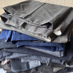 May include: A stack of folded trousers in various shades of gray, blue, and black. The top layers are tailored pants with cuffs, while the lower layers appear to be fabric swatches. One pair of pants has a "Banana Republic" label.