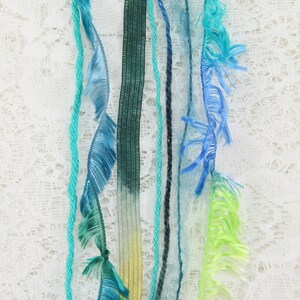 May include: Assortment of colorful yarn and ribbon strands with fringed edges, hanging against a white lace background.