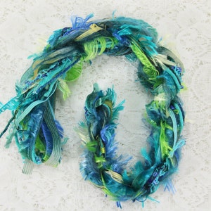 May include: A bundle of colorful yarn in shades of blue, green, and white. The yarn is made of a variety of textures, including fuzzy, silky, and ribbon-like strands.