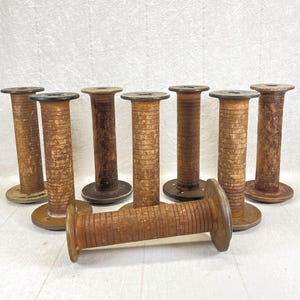 May include: A collection of eight antique wooden spools, each with a cylindrical body and a circular base and top. The spools are various shades of brown, with visible wood grain and signs of age. One spool lies horizontally in the foreground.