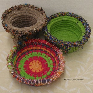 May include: Three colourful woven baskets with beaded trim. The baskets are made of felt and have a circular shape. The largest basket is green, the medium basket is brown, and the smallest basket is red, orange, and green.