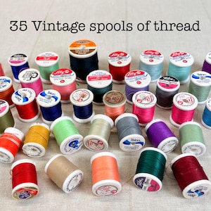 May include: A collection of 35 vintage spools of thread in various colors including red, blue, green, pink, yellow, and black. Each spool features a white label on top with brand names like Talon and Lily, and the text 35 Vintage spools of thread.