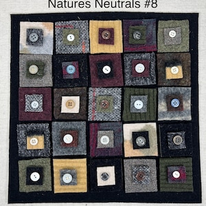 May include: A black framed square art piece with the title "Natures Neutrals #8". The piece is made up of 36 small squares of different fabrics and colors, each with a button in the center. The buttons are various colors and sizes.