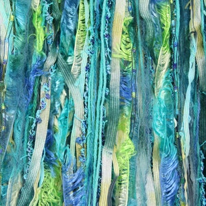May include: A close-up of a wall hanging made of various shades of blue, green, and white yarn. The yarn is woven together to create a textured and colorful design.