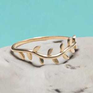 May include: A gold ring featuring a delicate leaf design. The ring is made from a thin band with a series of small leaves that create a continuous pattern.