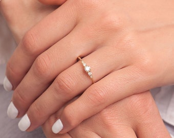 May include: A delicate gold ring with a small round diamond in the center and two smaller diamonds on either side.