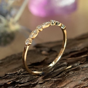 May include: A delicate gold band ring with a row of small, round, clear gemstones set in a curved design.