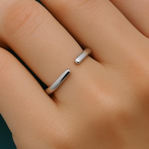 May include: A silver open ring with a simple, minimalist design. The ring is made of a single, continuous piece of metal that is bent into a circle with a gap at the top.