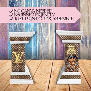 May include: Two decorative white and brown columns with a repeating pattern and gold accents. One column features a gold letter "L", and the other has a cartoon image of a woman with the text "Sassy, classy and a little bad assy". The columns are on a wooden surface.