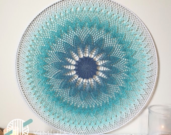 May include: A large, round, crocheted wall hanging with a gradient of blue and green colors. The center of the hanging is a darker blue color and the outer edges are a lighter white color.