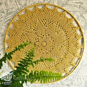 May include: A circular mustard yellow crochet wall hanging featuring an intricate mandala pattern with a star-shaped outer edge. The crochet piece is mounted on a matching mustard yellow circular frame, creating a sun-like design with openwork.
