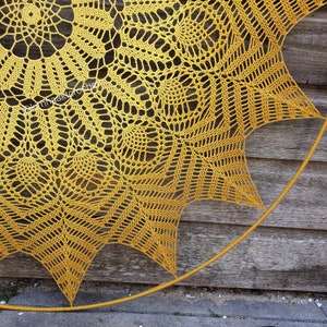 Puede incluir: Un gran doily de ganchillo amarillo con un dise&ntilde;o circular. El doily est&aacute; sujeto a un aro de metal y est&aacute; colgado en una pared de madera.