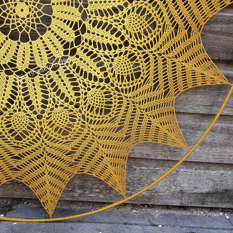 Puede incluir: Un gran doily de ganchillo amarillo con un dise&ntilde;o circular. El doily est&aacute; sujeto a un aro de metal y est&aacute; colgado en una pared de madera.