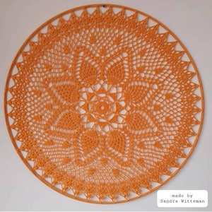 Puede incluir: Un gran encaje de ganchillo redondo de color naranja con un patr&oacute;n detallado e intrincado. El encaje est&aacute; hecho con un solo punto de ganchillo y tiene una apariencia delicada y de encaje. "made by Sandra Witteman" est&aacute; escrito en texto negro en la parte inferior de la imagen.
