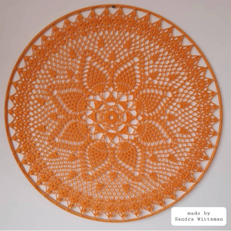 Puede incluir: Un gran encaje de ganchillo redondo de color naranja con un patr&oacute;n detallado e intrincado. El encaje est&aacute; hecho con un solo punto de ganchillo y tiene una apariencia delicada y de encaje. "made by Sandra Witteman" est&aacute; escrito en texto negro en la parte inferior de la imagen.