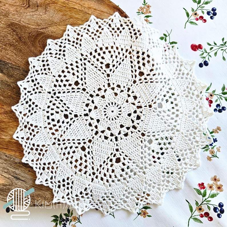 May include: A round, off-white crochet doily featuring an intricate, radiating starburst pattern with openwork stitches and a scalloped edge. The design consists of a central circular motif surrounded by repeating geometric segments.
