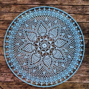 Puede incluir: Un gran encaje redondo de ganchillo azul con un dise&ntilde;o intrincado y de encaje. El encaje est&aacute; colgado en una pared de madera.