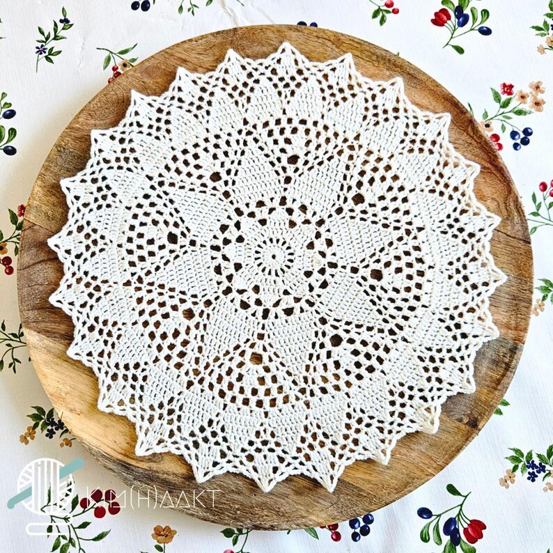 May include: A round, off-white crochet doily featuring an intricate, star-shaped geometric pattern with openwork stitching and a pointed, scalloped edge. The handmade textile piece displays a central circular motif radiating outward in a symmetrical design.