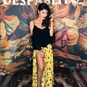 May include: A black sleeveless top with thin straps and a yellow floor-length skirt featuring a small red and green floral pattern and a high side slit, paired with white sneakers. The background displays the text DELIA GRASU XXL DESPABLITO.