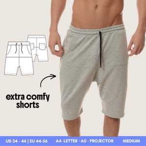 Może przedstawiać: Jasnoszare szorty z elastycznym pasem, czarnym sznurkiem, kieszeniami bocznymi i obniżonym krokiem. Obraz zawiera rysunek techniczny, tekst extra comfy shorts oraz oznaczenia rozmiarów US 34-46, EU 44-56.