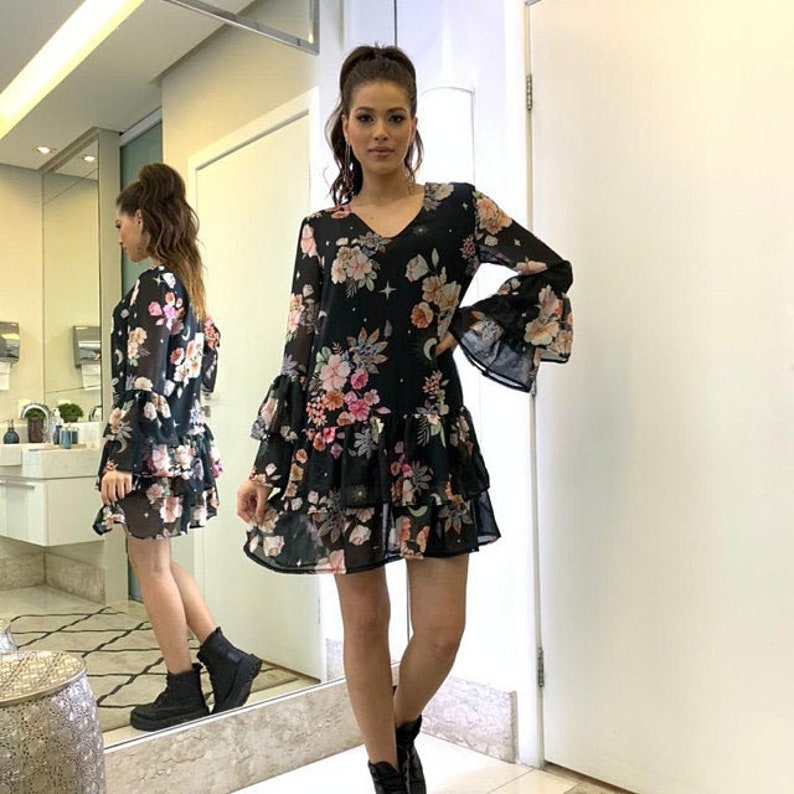 May include: A black floral print dress with long sleeves and a ruffled hem. The dress has a V-neckline and a sheer fabric.