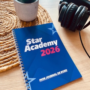 Op de afbeelding: Een spiraalgebonden notitieboek met een blauwe kaft met de witte tekst Star Academy, het roze jaartal 2026 en de witte tekst MON JOURNAL DE BORD. Het ontwerp bevat witte steromtrekken op een donkerblauwe achtergrond met geometrische vormen.