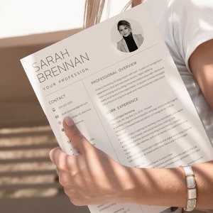 May include: A black and white resume with the name Sarah Brennan at the top. The resume lists her contact information, professional overview, work experience, and education. The resume is held by a person's hand.