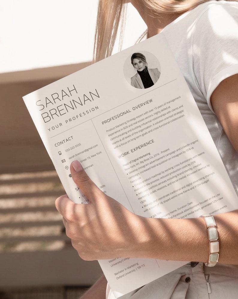 May include: A black and white resume with the name Sarah Brennan at the top. The resume lists her contact information, professional overview, work experience, and education. The resume is held by a person's hand.
