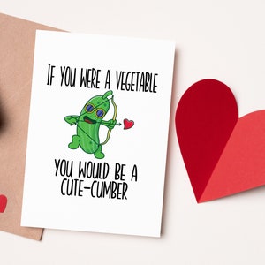 May include: A white card with a green cartoon cucumber holding a bow and arrow. The card reads "If you were a vegetable you would be a cute-cumber".