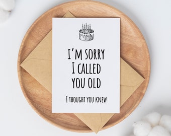 Op de afbeelding: Een witte kaart met een zwart-witte illustratie van een verjaardagstaart met kaarsen. De tekst op de kaart luidt: "Het spijt me dat ik je oud heb genoemd. Ik dacht dat je het wist."