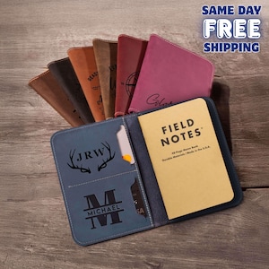 May include: A collection of leather notebooks and covers in various colors, including brown, burgundy, and blue. One blue cover is open, revealing a Field Notes memo book and card slots. The covers are personalized with initials and names.