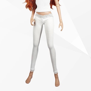Könnte beinhalten: Eine Puppe in einem weißen Rippen-Tanktop und hellgrauen Leggings. Die Leggings haben eine Spitzentrimmung an Taille und Knöcheln. Die Puppe hat rotes Haar und trägt goldene Armbänder.