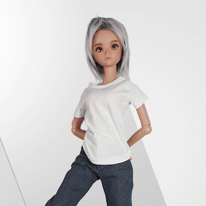 Könnte beinhalten: Eine Puppe mit grauem Haar, die ein weißes T-Shirt und blaue Jeans trägt. Die Puppe hat einen neutralen Ausdruck und posiert mit den Händen hinter dem Rücken. Der Hintergrund ist schlicht weiß.