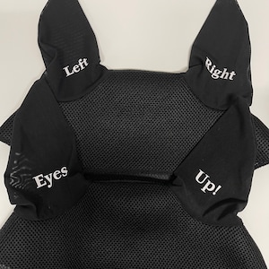 May include: Black fly bonnet with white text reading "Left", "Right", "Eyes", and "Up!". The bonnet features a mesh design and is trimmed with white lace. The text "Fly bonnets with reminder messages for the rider! All ear letters are in white lettering only." is at the top.