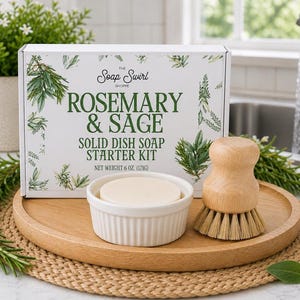 May include: A white rectangular box labeled The Soap Swirl Shoppe Rosemary & Sage Solid Dish Soap Starter Kit Net Weight 6 oz. (171g) with a white ceramic ramekin containing a solid soap disc and a wooden dish brush on a round wooden tray.