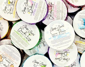 May include: A collection of round shower steamers from The Soap Swirl Shoppe, each wrapped in colorful foil with a white label. The labels feature various scent names like Bedtime, Breathe Easy, and Snow Flurries, with a net weight of 1.5 ounces.